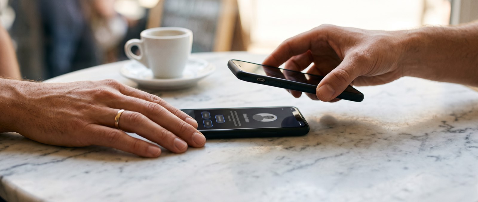 One phone lowered onto another on a cafe table to swap details with a tap