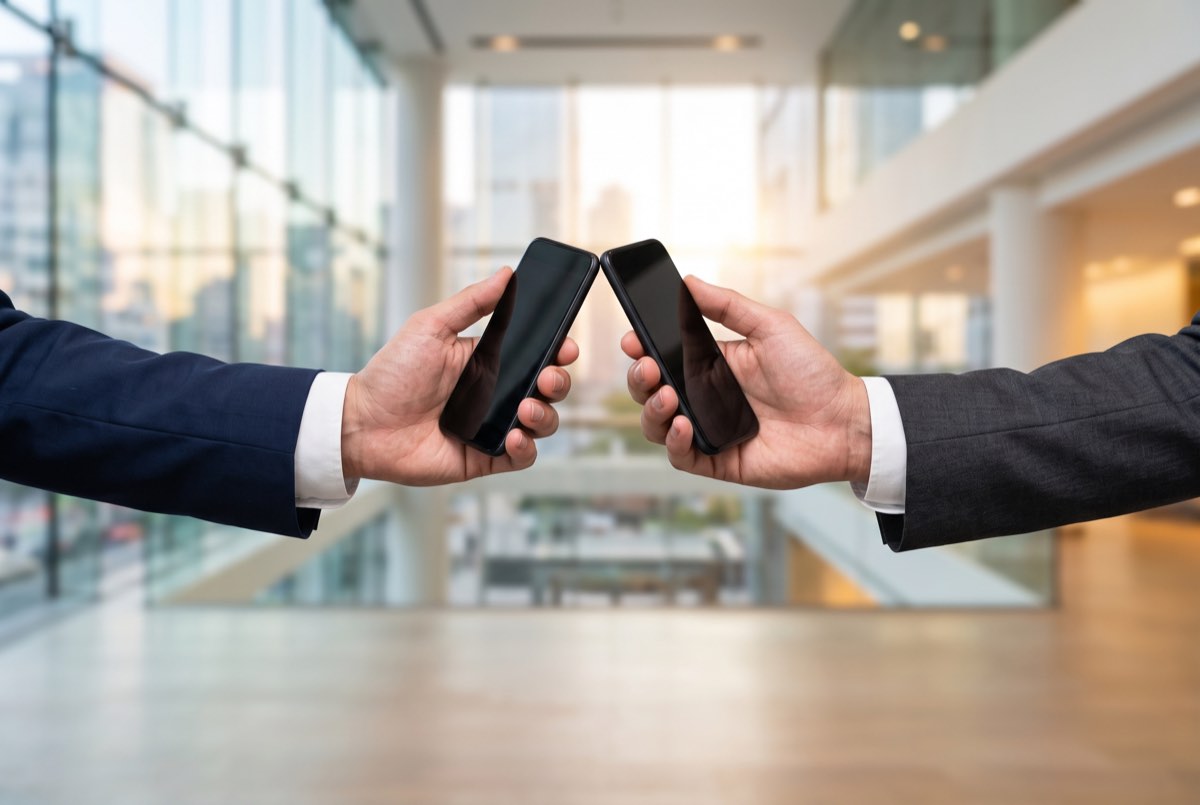 Two people holding out their phones to each other to swap details, as you would offer a business card