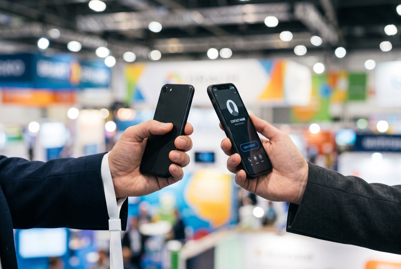 Two people tapping their phones together to swap details on a trade-expo floor